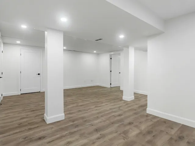 Ausgebauter heller Raum mit verkleideten Stützen, Deckenleuchten und neuem Boden
